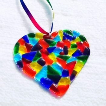 A beautiful, bright and colourful large rainbow heart made using rainbow coloured glass, hanging with rainbow ribbon.