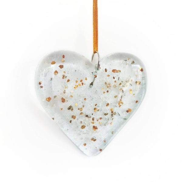 Cremation Ashes fused inside a clear hanging heart with a sprinkling of gold glitter, on a white background.