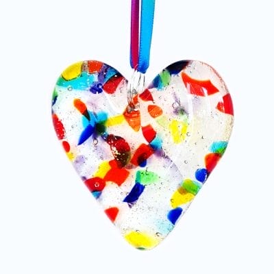 Cremation Ashes fused inside a clear glass heart with small pieces of coloured glass, on a white background.
