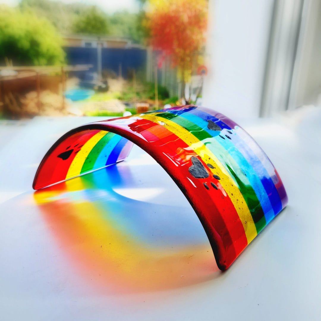 A glass Rainbow Bridge with black dog pawprints hand drawn in enamel with cremation ashes fused inside the glass.