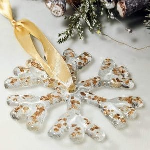 A handmade fused glass gold flecked snowflake on a white background