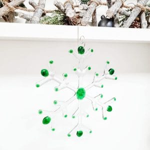 A green and clear fused glass large snowflake hanging on a white background