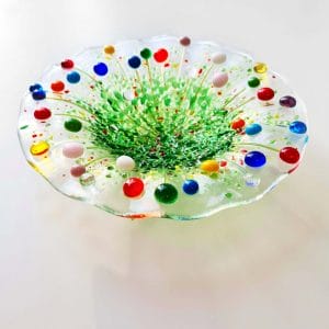 A handmade fused glass bowl with various coloured flowers with a fluted edge design