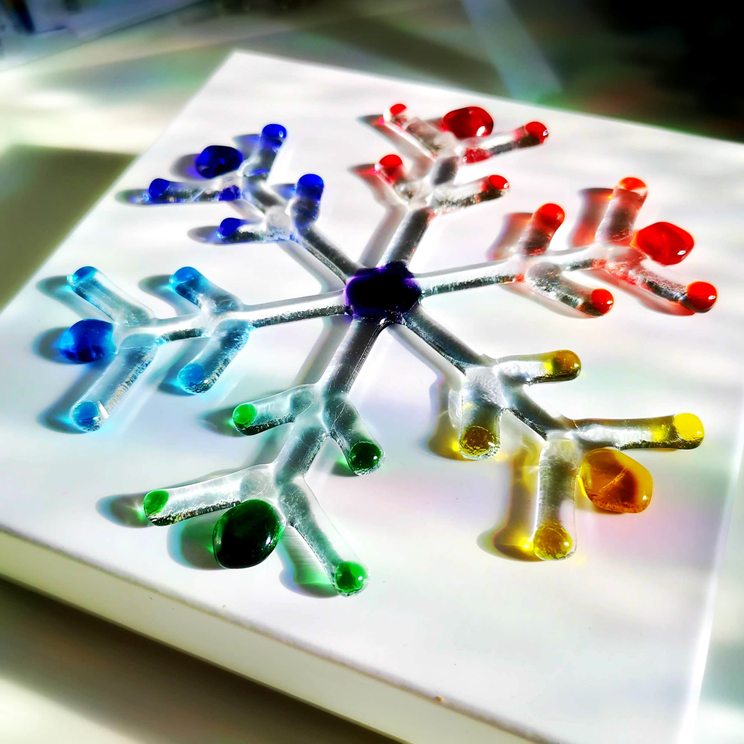 A rainbow and clear fused glass large snowflake with a white background.