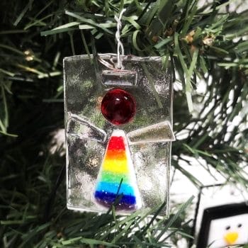 A glass angel with rainbow colours on a green christmas tree