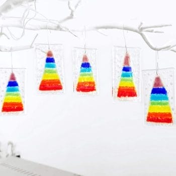 5 fused glass hanging christmas decorations featuring a rainbow christmas tree and white "snow" hanging from a white tree branch.