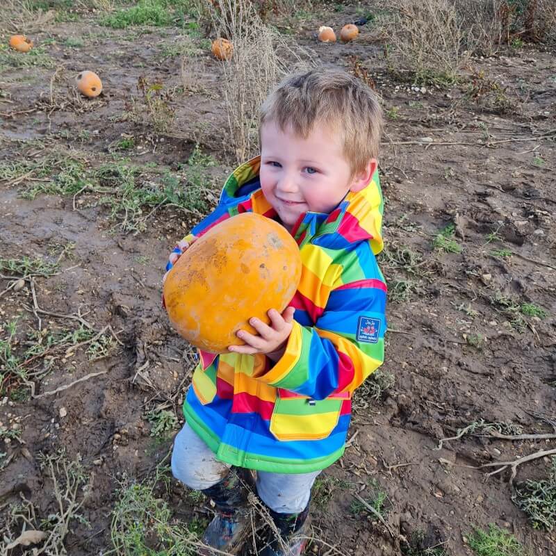 My son, Roux, holding a large orange pumpkin, wearing a Rainbow coat.